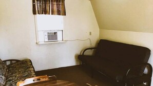 Una habitación con ventana, un equipo de aire acondicionado, una mesa de madera y dos sillas.