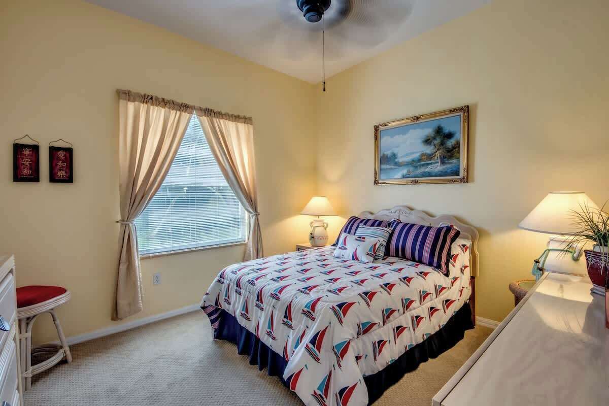 Un dormitorio con cama, dos lámparas de noche, ventana con cortinas, un cuadro en la pared y una mesita con una planta.