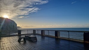 Eine Holzterrasse mit Geländer, die auf einen Küstenabhang und den Ozean blickt.
