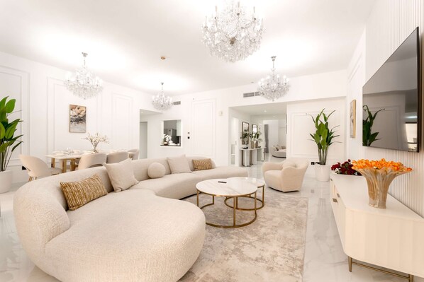 A spacious living room with a large L-shaped sectional sofa, a round coffee table, and a white console table with a vase of flowers. - Stayshort - Modern 4 Bed Apartment in JBR That Sleeps 8 (Dubai)