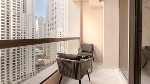 Un balcón con vistas a edificios altos, una silla de mimbre y una pequeña mesa.