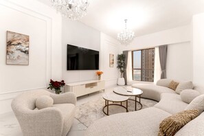 A modern living room with a large flat-screen TV, a white console table, a beige sofa, and a round coffee table. - Stayshort - Modern 4 Bed Apartment in JBR That Sleeps 8 (Dubai)