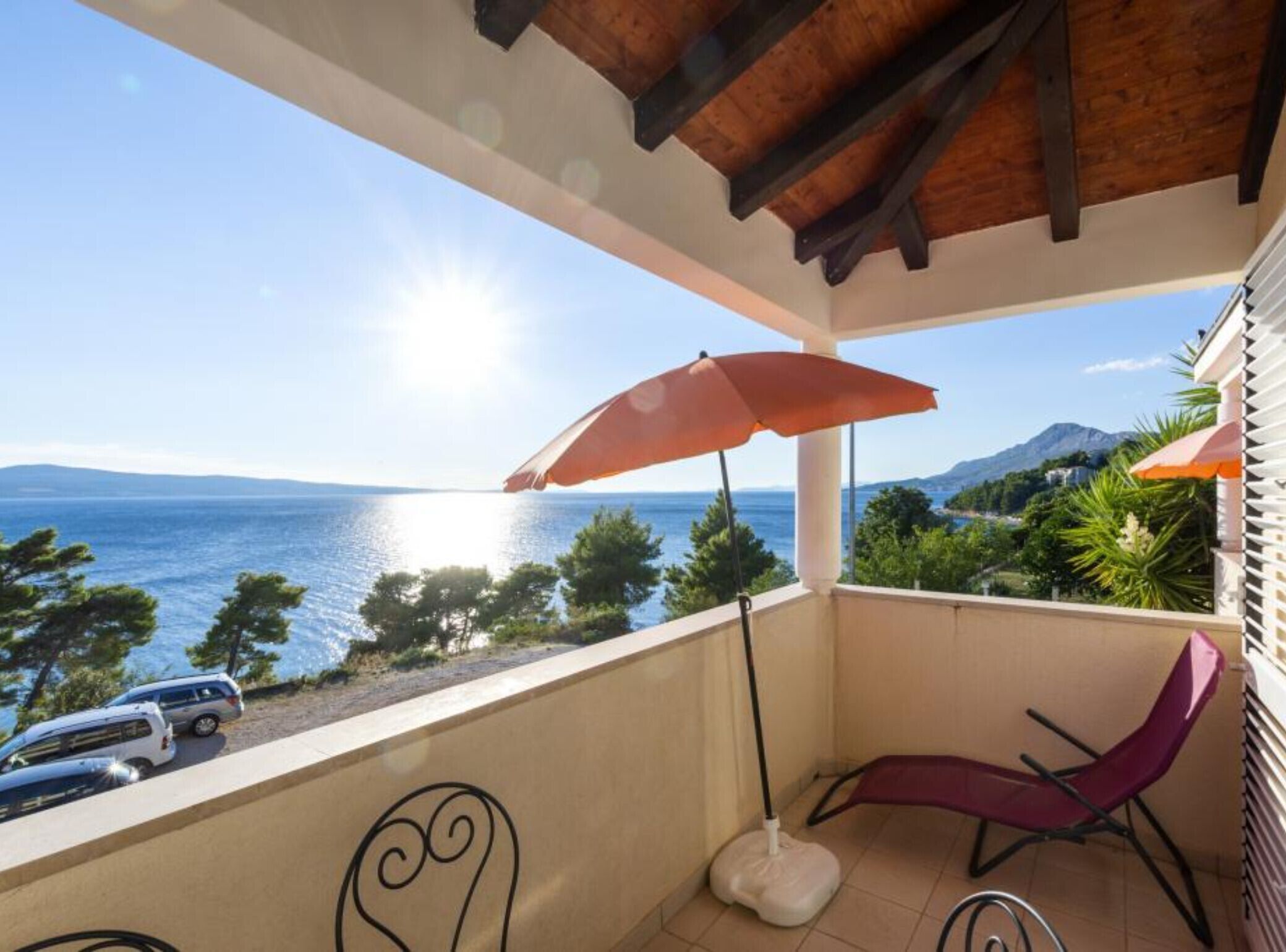 Un balcón con vista al mar, un coche aparcado y una silla.