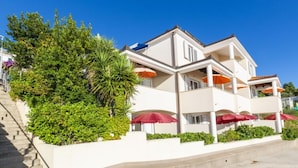 A multi-story hotel with balconies, outdoor seating with umbrellas, and a staircase leading to the entrance. - Standard One Bedroom Apartment with Sea View and Terrace (Stanici)