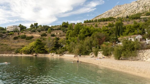 Zona costera con aguas cristalinas, una playa arenosa y edificios en una ladera.