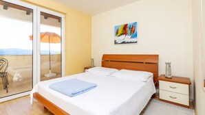 Un dormitorio con cama, mesita de noche, silla, un cuadro y vistas a través de un ventanal corredizo.