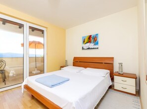 Ein Schlafzimmer mit einem Bett, einem Nachttisch, einem Sessel, einem Gemälde und Blick durch eine Schiebetür.