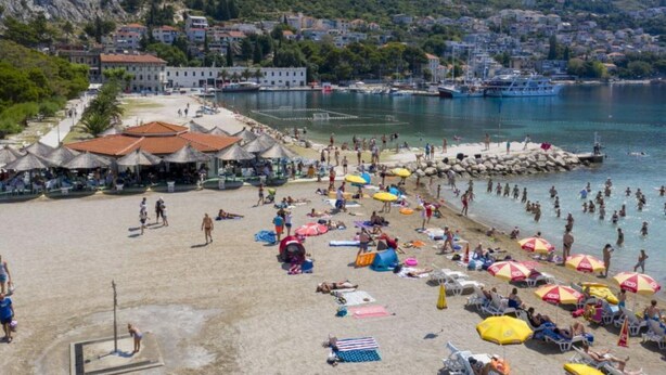 Een strand met parasols, mensen en een uitzicht op de stad en bergen op de achtergrond.