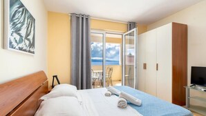 Een hotelkamer met een bed, een houten bankje, een televisie en een balkon met uitzicht.