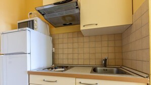 Een kleine keuken met een witte koelkast, een magnetron, een fornuis en een spoelbak.
