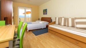 Een slaapkamer met een bed, een sofa, een eettafel en uitzicht op zee door een schuifdeur.