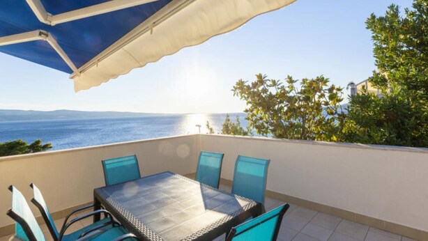 Ein Balkon mit Tisch und Stühlen, der auf ein Gewässer und Grün blickt.
