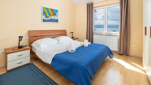 Ein Schlafzimmer mit Bett, Nachttisch, Lampe, einem Fenster mit Vorhängen und einem Bild an der Wand.