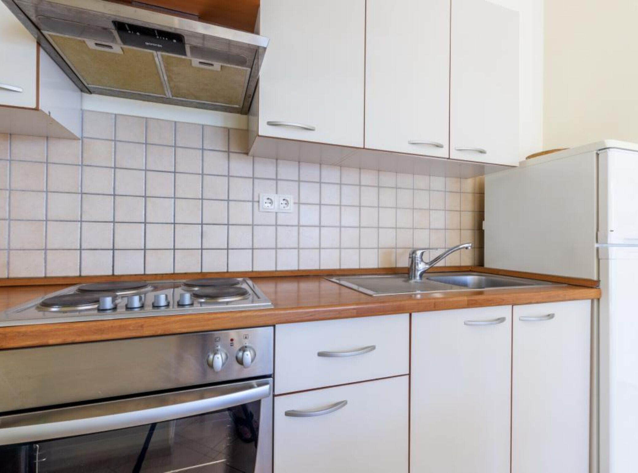 Una cucina con mobili bianchi, un piano cottura in acciaio inossidabile, un lavello e un frigorifero bianco.