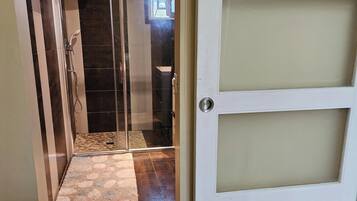 Un baño con cabina de ducha de vidrio, una puerta blanca con paneles esmerilados y un perchero con toallas rojas.