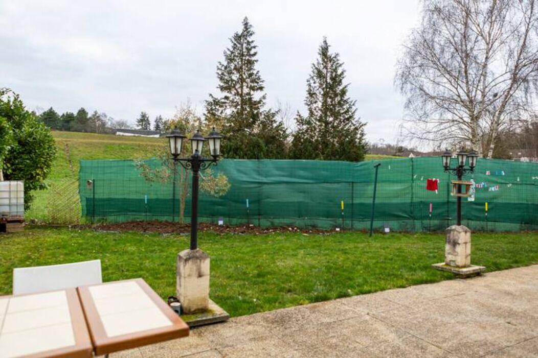 A patio area with a table and chairs, a lamp post, and a green netted fence in the background.