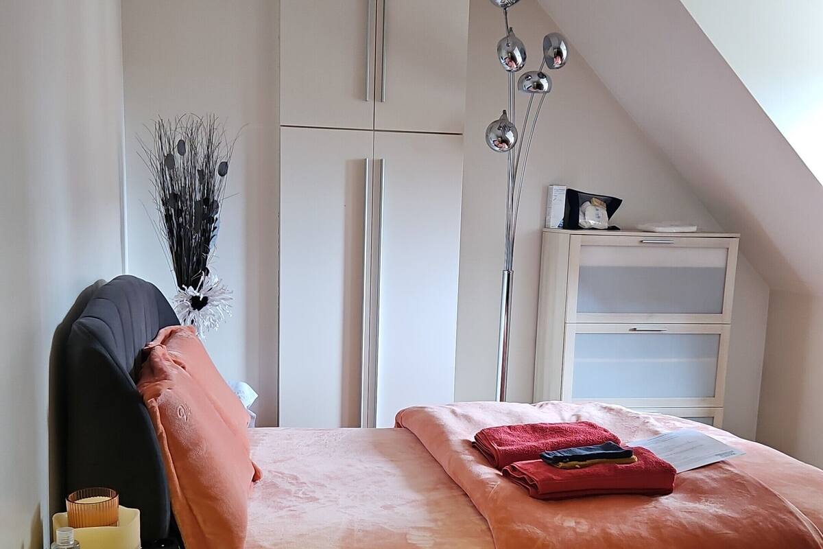 Et soveværelse med seng, natbord, lampe, garderobeskab og ovenlysvindue.