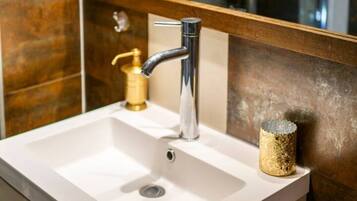 A bathroom sink with a chrome faucet, a gold soap dispenser, and a textured gold container.