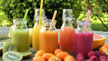Four glass bottles with straws, each containing a different colored smoothie, surrounded by sliced fruits.