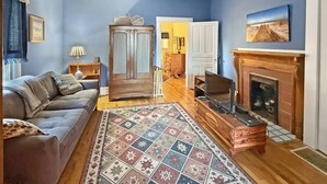 Ein Wohnzimmer mit einer Couch, einem Fernseher, einem Kamin, einem gemusterten Teppich und einem Holzkasten.