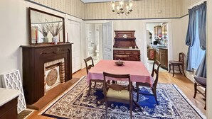 Ein Esszimmer mit einem rot karierten Tisch, Holzsesseln, einer Chandelüster, einem Kamin und einem gemusterten Teppich.