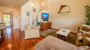 A spacious living room with a wooden floor, a sofa, a coffee table, and a television on a wooden cabinet. - Bright Island Suite w/ Airy Lanai and Stunning Sunset Views - Near Waikoloa Golf (Hawaii County)
