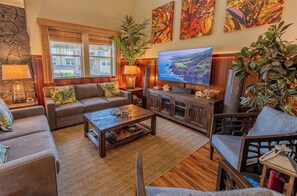 A cozy living room with a sofa, coffee table, and TV. There are plants, a lamp, and a bookshelf. - Enjoy Stunning Views at Relaxing Island-Style Suite with Balcony and Living Area (Hawaii County)