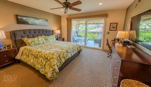 A bedroom with a large bed, a ceiling fan, a sliding glass door to a balcony, and a dresser with a mirror. - Experience Stunning Views from Your Island-Style Suite w/ Kitchen & Living Area (Hawaii County)