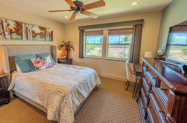 A bedroom with a bed, a dresser, a desk, and a window with a view of palm trees. - Experience Stunning Views from Your Island-Style Suite w/ Kitchen & Living Area (Hawaii County)