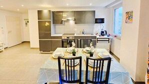 A modern kitchen with stainless steel appliances, a dining area with a table set for four, and a window with a city view. - Exceptional 1BR Apartment in center (Luxembourg City)