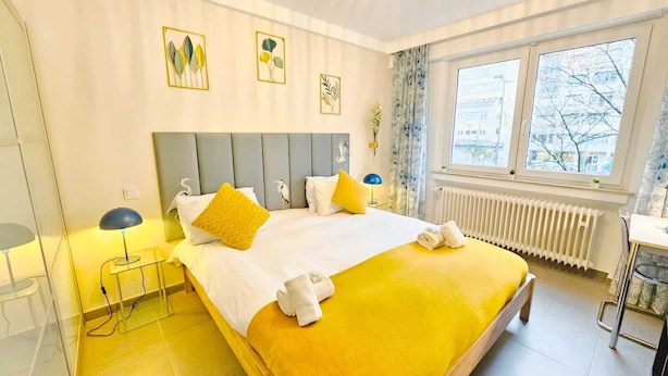 A hotel room with a bed, bedside tables, a radiator, and a window with a view. - Exceptional 1BR Apartment in center (Luxembourg City)