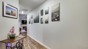 Een gang met ingelijste foto’s aan de muur, een houten tafel met een plant en een plafondlamp.