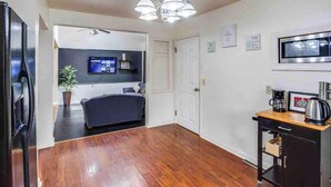 A modern living room with a dark sofa, a flat-screen TV, a potted plant, and a coffee station. - Enjoyable Home by Airport and Dwtn (Rochester)