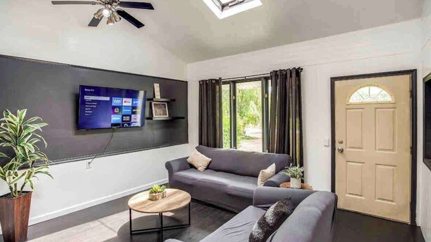 A modern living room with a grey sofa, a coffee table, and a flat-screen TV mounted on the wall. - Enjoyable Home by Airport and Dwtn (Rochester)