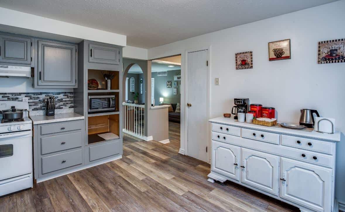Une cuisine avec des meubles gris, un four à micro-ondes et une cuisinière. Un escalier mène à une autre pièce.