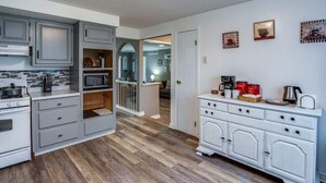 Une cuisine avec des meubles gris, un four à micro-ondes et une cuisinière. Un escalier mène à une autre pièce.
