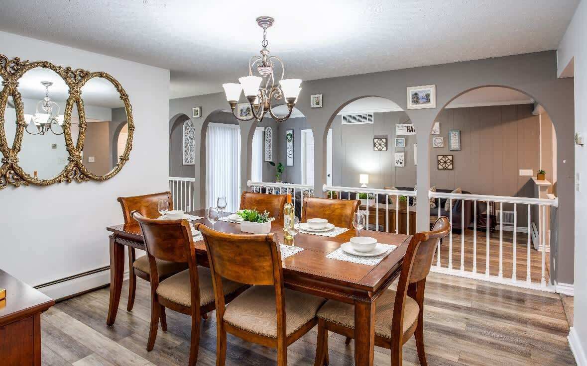Un coin repas avec une table en bois dressée pour quatre personnes, entourée de chaises. Un lustre est suspendu au-dessus de la table, et la pièce présente un design moderne avec des murs gris et un plancher en bois.