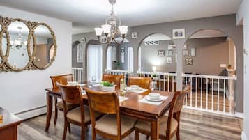 Un coin repas avec une table en bois dressée pour quatre personnes, entourée de chaises. Un lustre est suspendu au-dessus de la table, et la pièce présente un design moderne avec des murs gris et un plancher en bois.