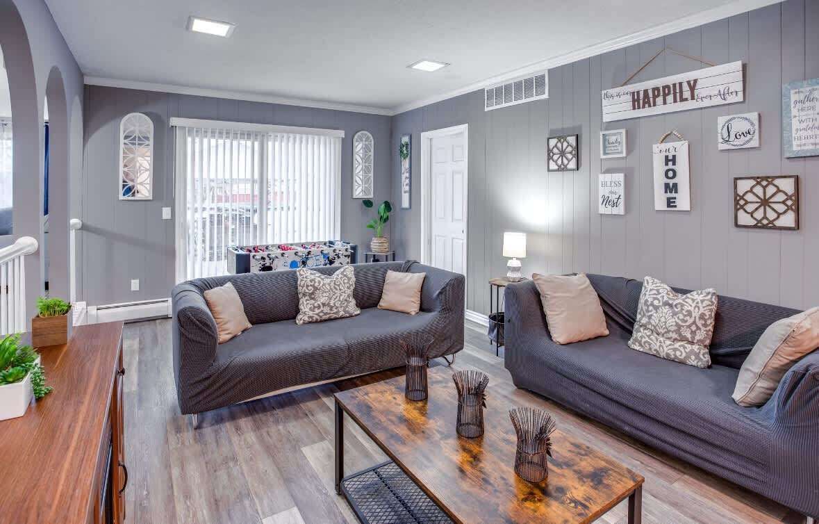 Un salon moderne avec deux canapés gris, une table basse en bois et des œuvres d’art décoratives accrochées au mur.