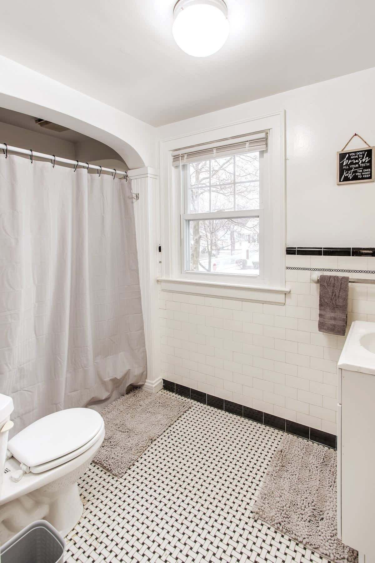 A bathroom with a toilet, shower curtain, window, and a towel rack.