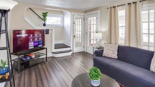 Ein modernes Wohnzimmer mit Flachbildfernseher, einer Couch, einem Couchtisch und einer Treppe zu einem anderen Raum.