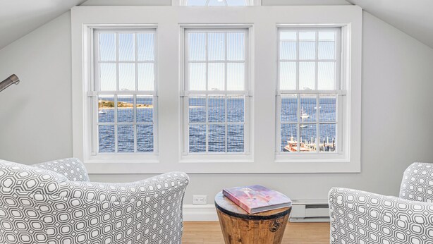 A room with three large windows overlooking the sea, a wooden barrel table, and patterned chairs. - The Eagle’s Nest Penthouse: 360° Views in the Heart of Watch Hill (Westerly)