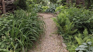 Ein Kiesweg schlängelt sich durch einen üppigen Garten mit verschiedenen Pflanzen und Bäumen.