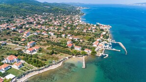 Vista aerea di una cittadina costiera con case, un porto turistico e acque blu cristalline.