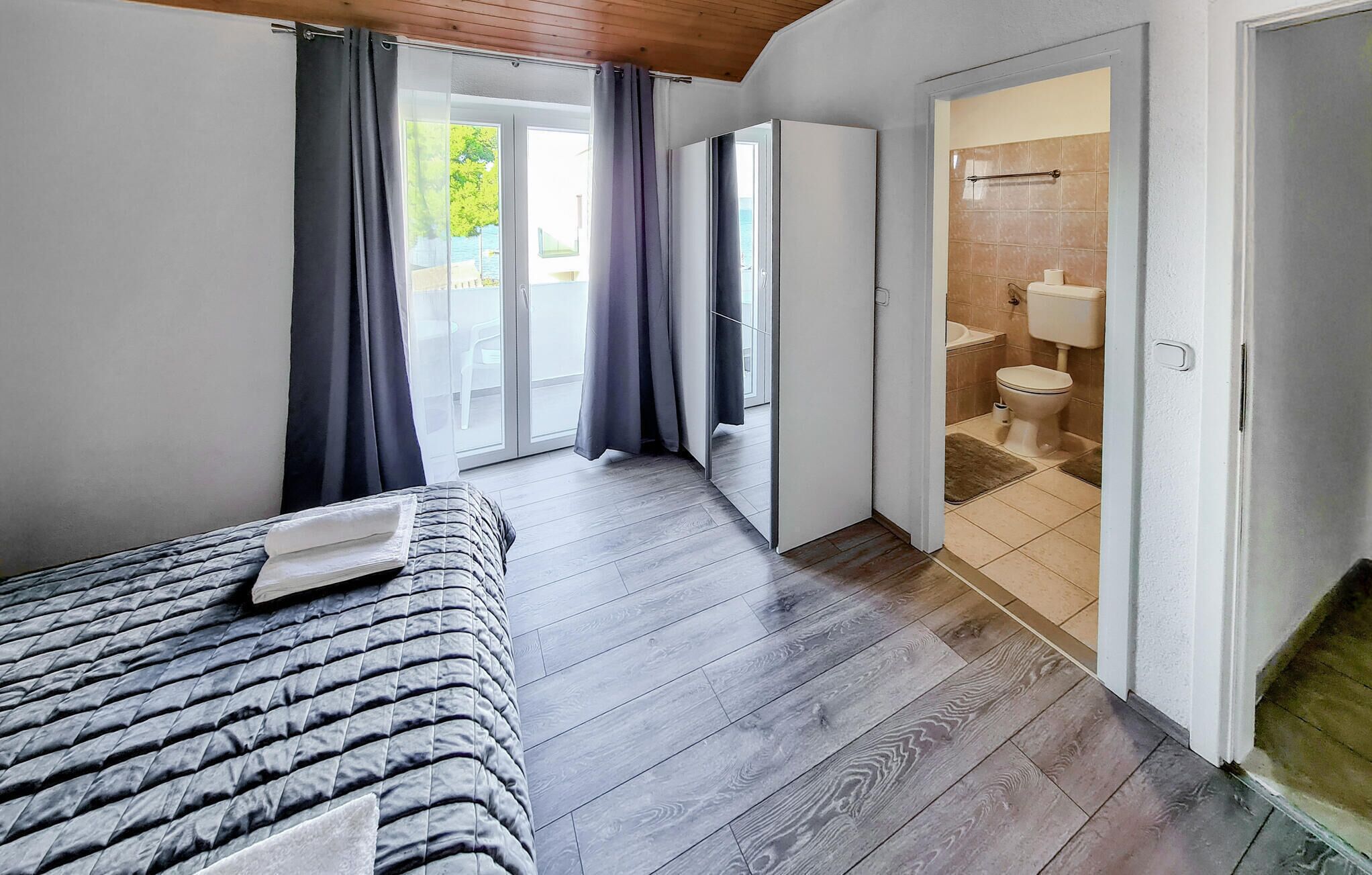 A bedroom with a bed, a bathroom with a toilet and sink, and a sliding glass door leading to an outdoor area.