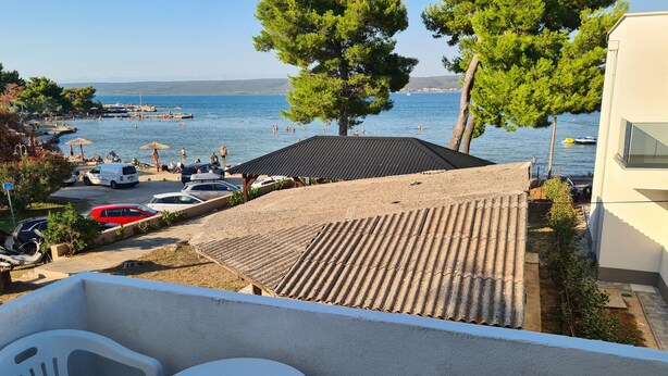 Un balcone con tetto in tegole affaccia su una spiaggia dove persone nuotano e ci sono barche nell'acqua.