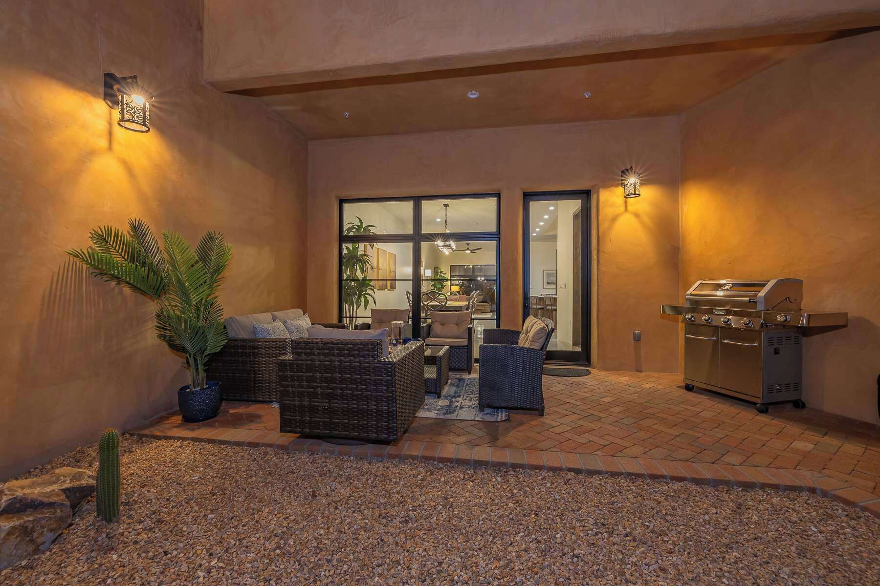 An outdoor patio with a grill, seating area, and a large window overlooking the interior.