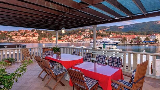 Um terraço com mesa e cadeiras vermelhas, com vista para uma orla com edifícios e um barco.