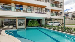 A modern apartment building with a swimming pool, balconies, and a view of the surrounding area. - Apt w/ Balcony, BBQ & Pool View Ano0209 (Cabo Frio)