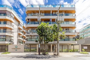 A modern multi-story residential building with balconies, a sign for 'Ocean Garden Condominium Complex', and a tree in the foreground.